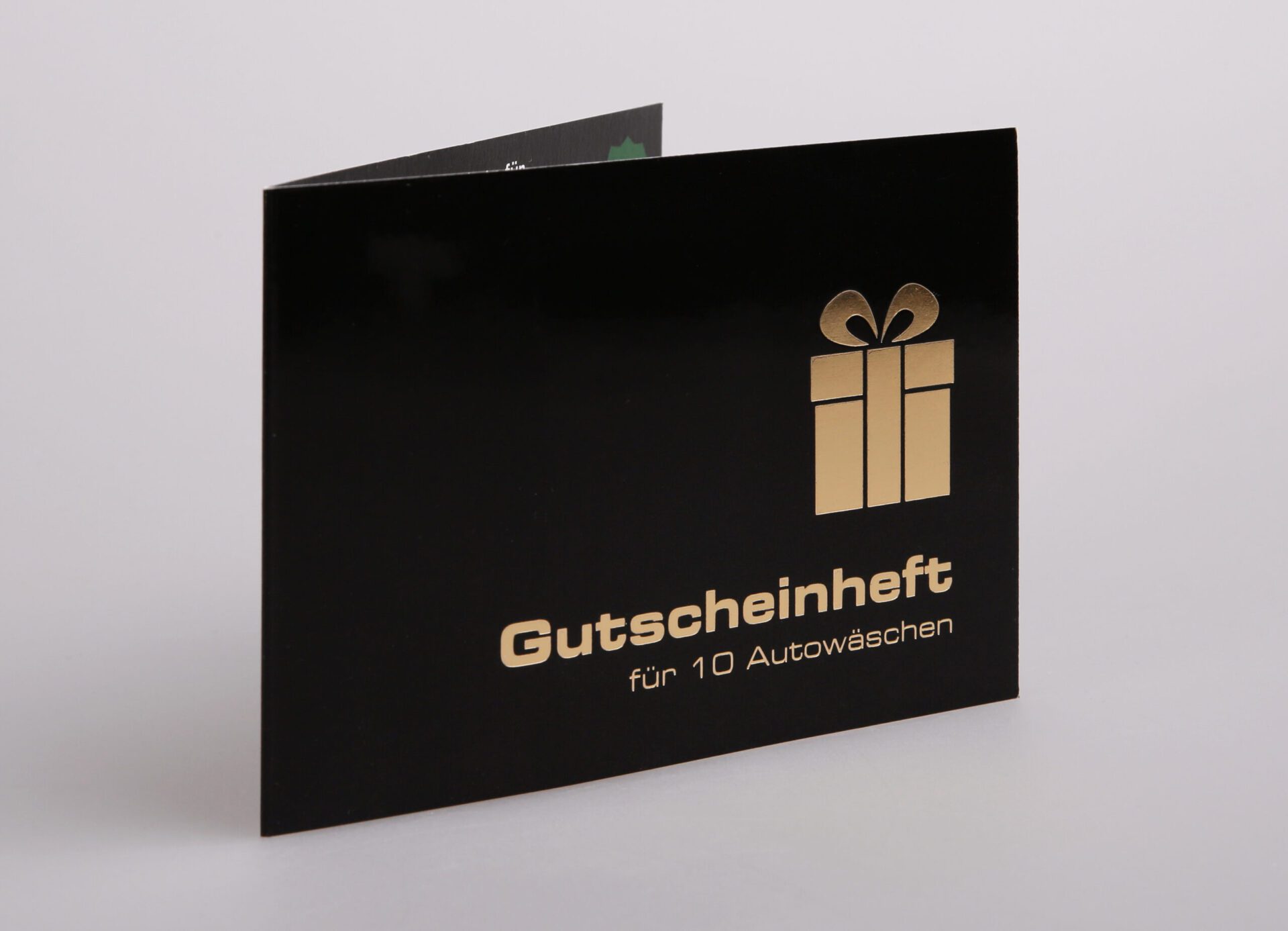 Schwarzes Gutscheinheft mit goldfarbener Heißfolienprägung und Geschenk-Symbol, Text „Gutscheinheft für 10 Autowäschen“.