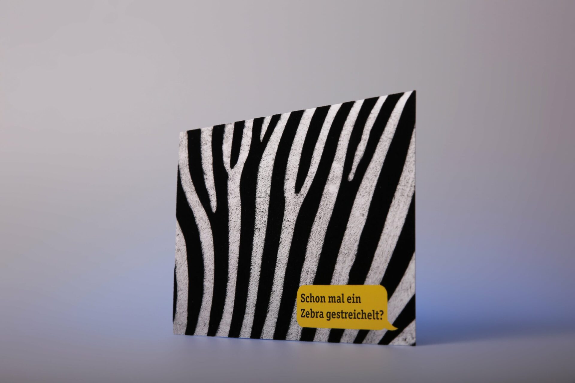 Postkarte mit Zebramuster und fühlbarem Flocklack, weiße samtige Streifen, gelbe Sprechblase mit Text Schon mal ein Zebra gestreichelt.