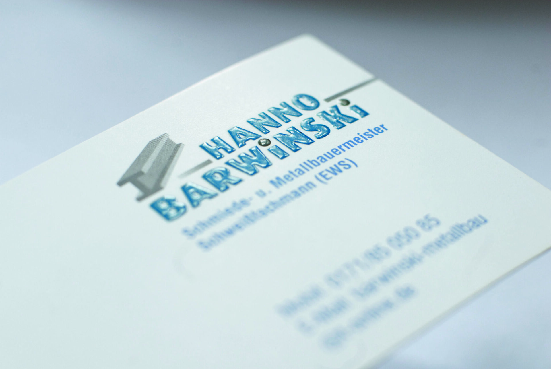 Visitenkarte mit glänzendem Relieflack, blauer erhabener Text Hanno Barwinski, Metallbaumeister, fühlbare Struktur.