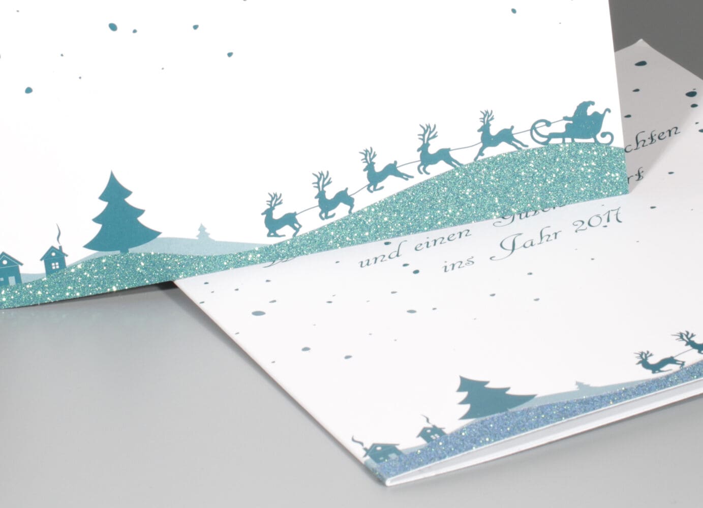 weihnachtliche Klappkarte mit Rentieren und Schlitten, veredelt mit blaugrünem Glitzerlack, winterliches Motiv.