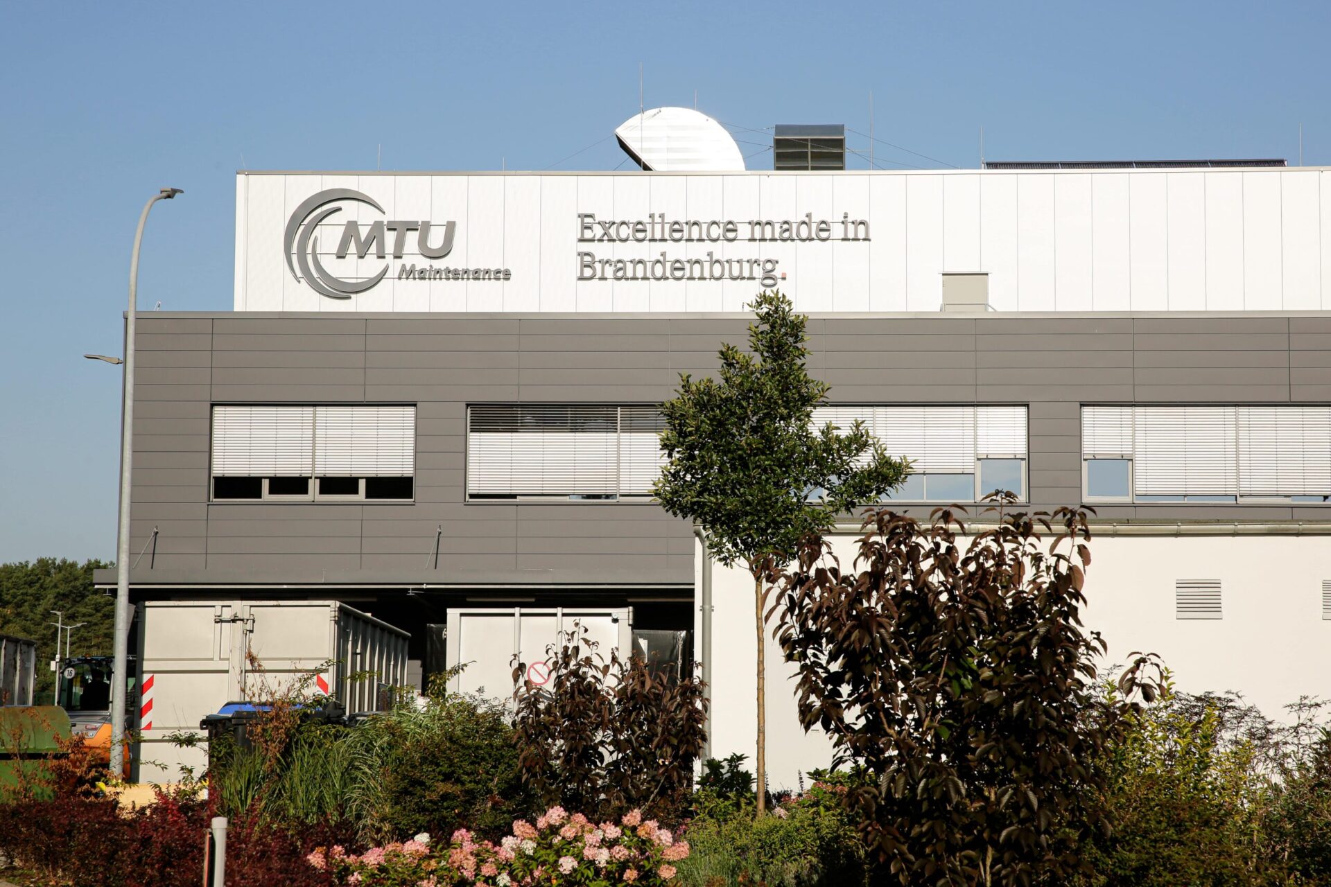 Außenwerbung mit 3D-Buchstaben MTU Brandenburg Große Außenwerbung mit 3D-Buchstaben „MTU Maintenance“ und „Excellence made in Brandenburg“ an der modernen Fassade eines Industriegebäudes.