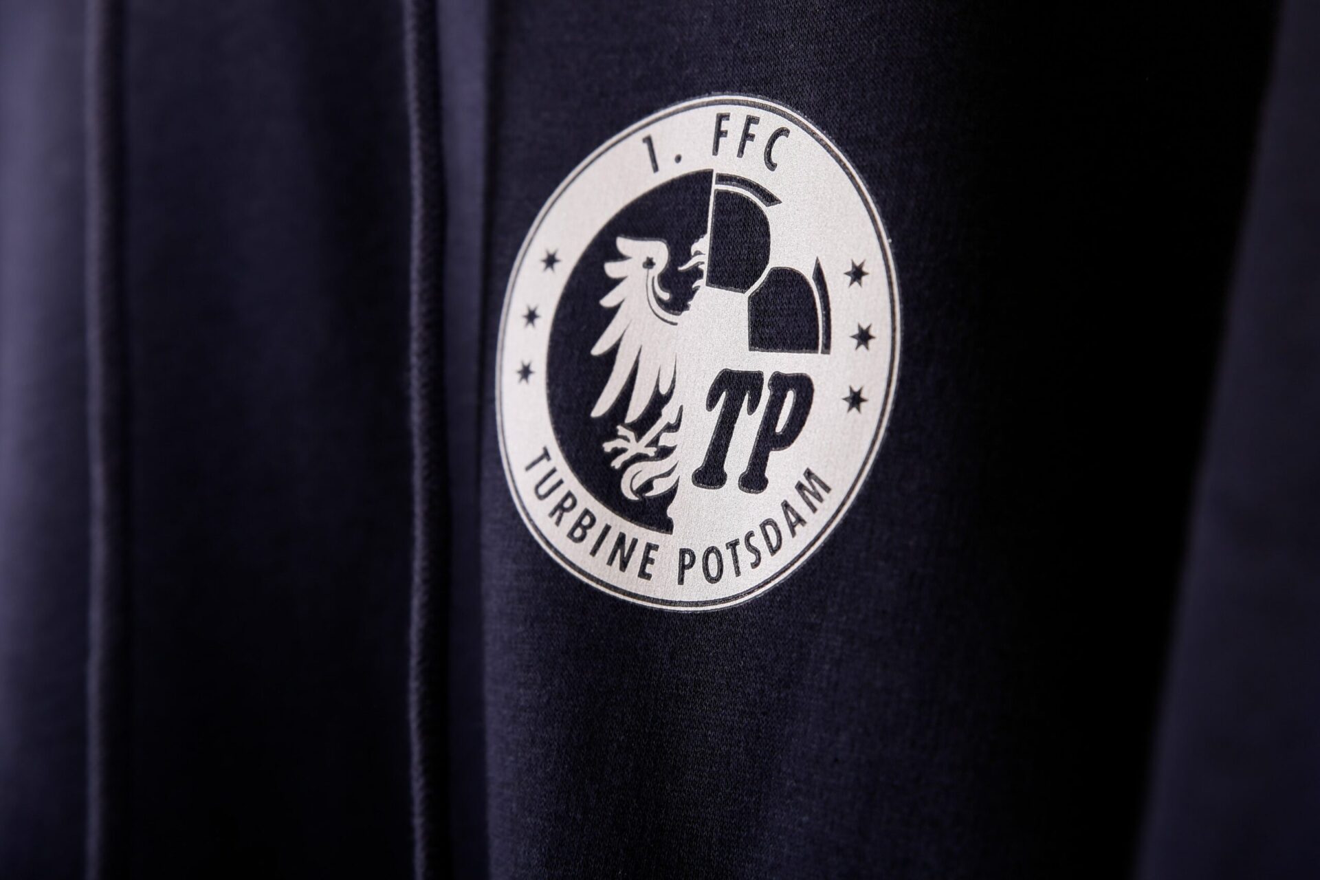 Weißer Logodruck von 1. FC Turbine Potsdam auf blauem Pullover