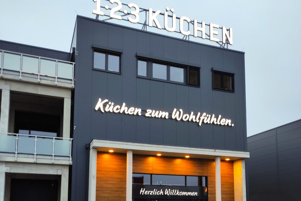 Beleuchtete Fassadenwerbung mit dem Slogan Küchen zum Wohlfühlen und Logo von 1-2-3 Küchen