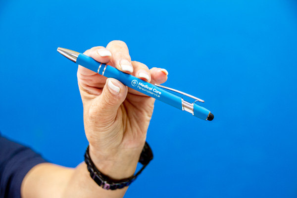 Hand hält einen blau-silbernen Kugelschreiber mit Lasergravur vor blauem Hintergrund.