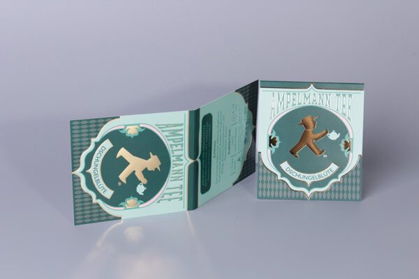 Hochwertige Verpackung des "Ampelmann Tee" Dschungelblüte mit Goldprägung und detailreichem Design.