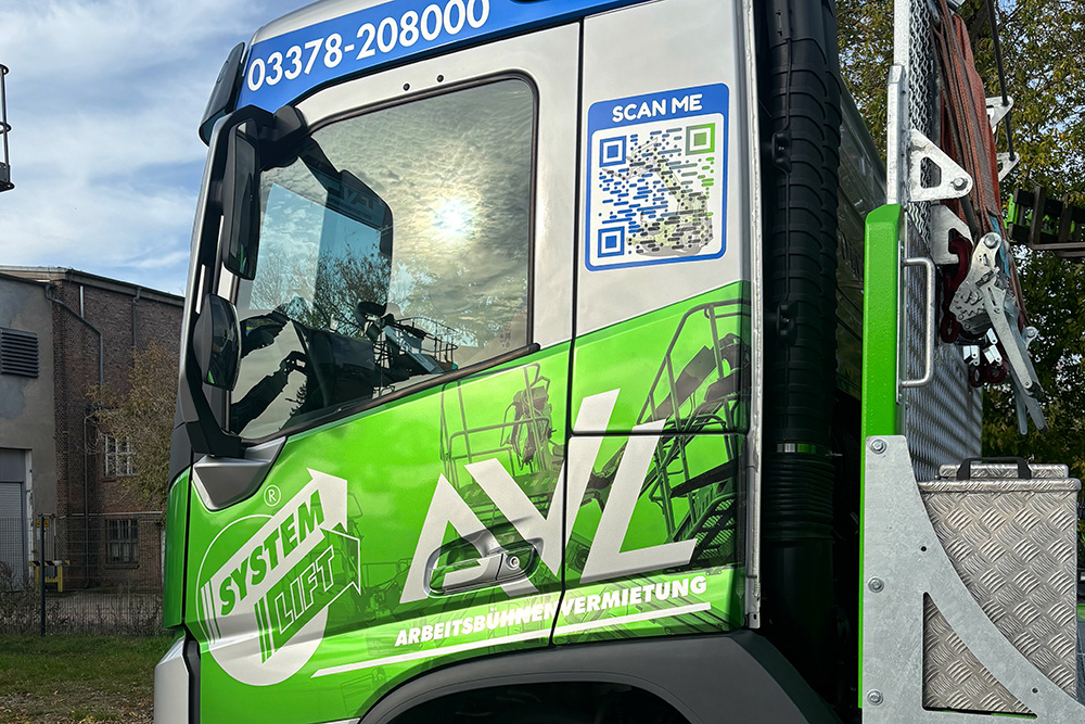 Teilfolierung_LKW_FahrerKabine_AVL_web Seitenansicht der Fahrerkabine eines AVL-Arbeitsbühnenfahrzeugs mit SYSTEM LIFT-Logo, Telefonnummer, QR-Code und grüner Folierung.