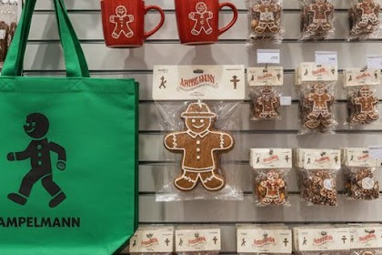 Merchandise-Wand mit grünem Ampelmann-Beutel, roten Tassen und verpackten Lebkuchenfiguren im Ampelmann-Design.