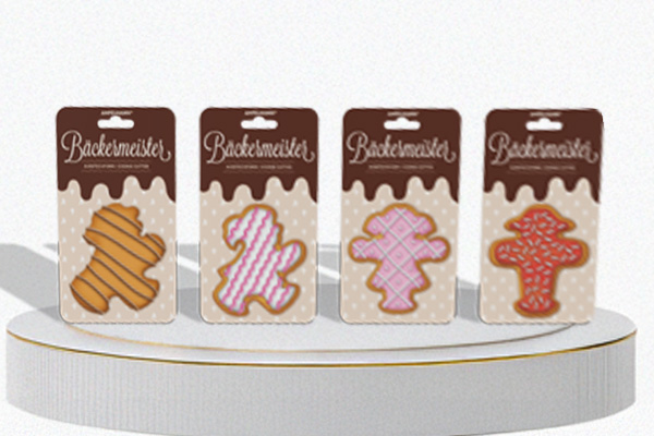 Vier Sattelreiter „Bäckermeister“ mit Euroloch auf Podest; je ein Keks-Motiv (verschiedene Zuckerguss-Designs) auf beige-braunem Layout.