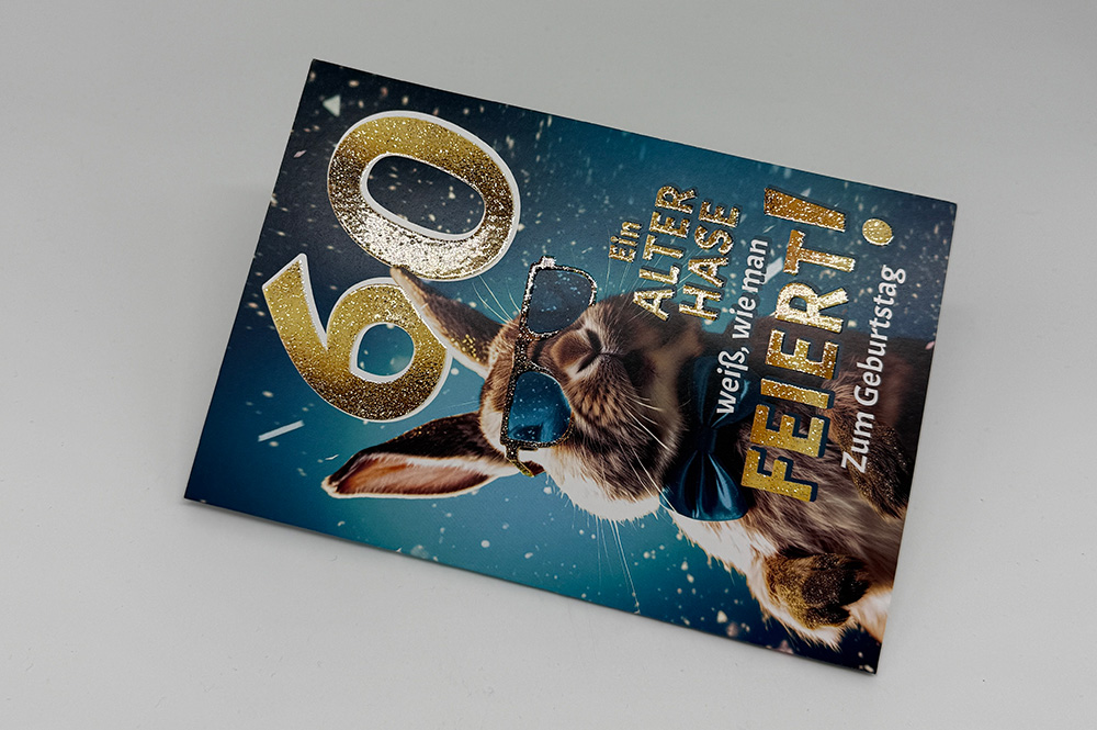 Geburtstagskarte „60“ mit goldfarbenem Glitzerlack, Hase mit blauer Brille auf blauem Hintergrund, funkelnde Akzente.