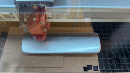 CO₂-Laser graviert Logo durch Farbabtrag auf einer lackierten Metallhülle; Vorrichtung fixiert das Etui präzise.