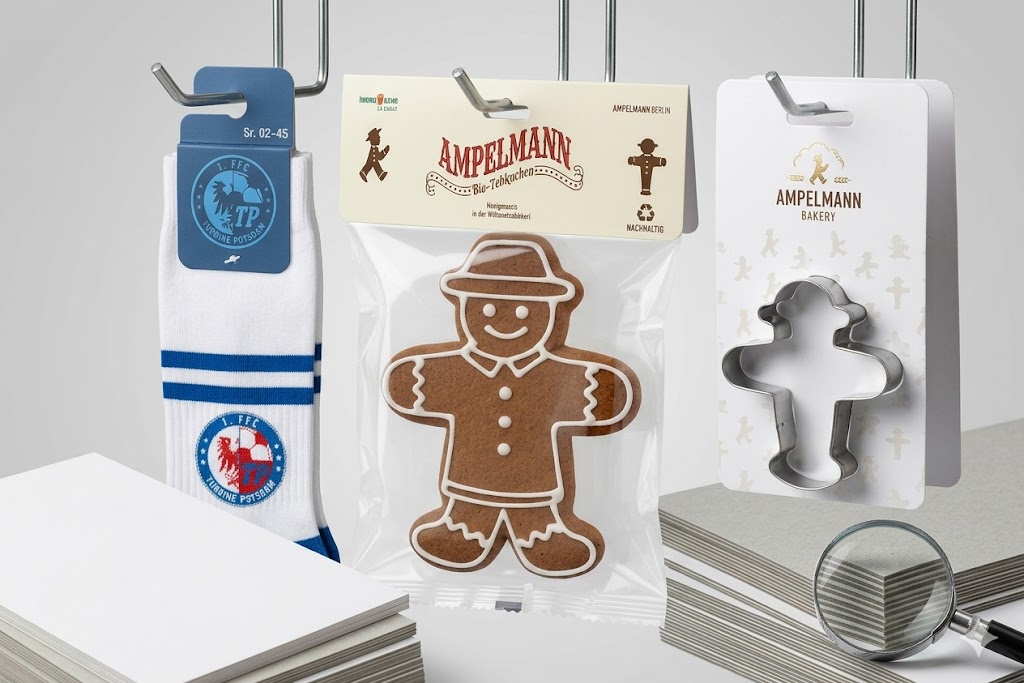 Sattelreiter-Verpackungsanhänger aus Karton an Metallhaken: Socken mit Aufhänger, verpackter Ampelmann-Lebkuchen und Ausstechform im Shop-Display.